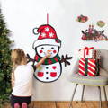 Little girl putting decorations on a felt Montessori Snowman that is hanging from a wall. 