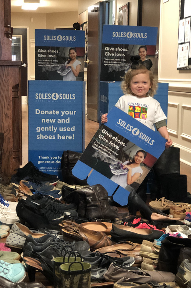 An Early Preschool student stands with over 80 pairs of shoes!