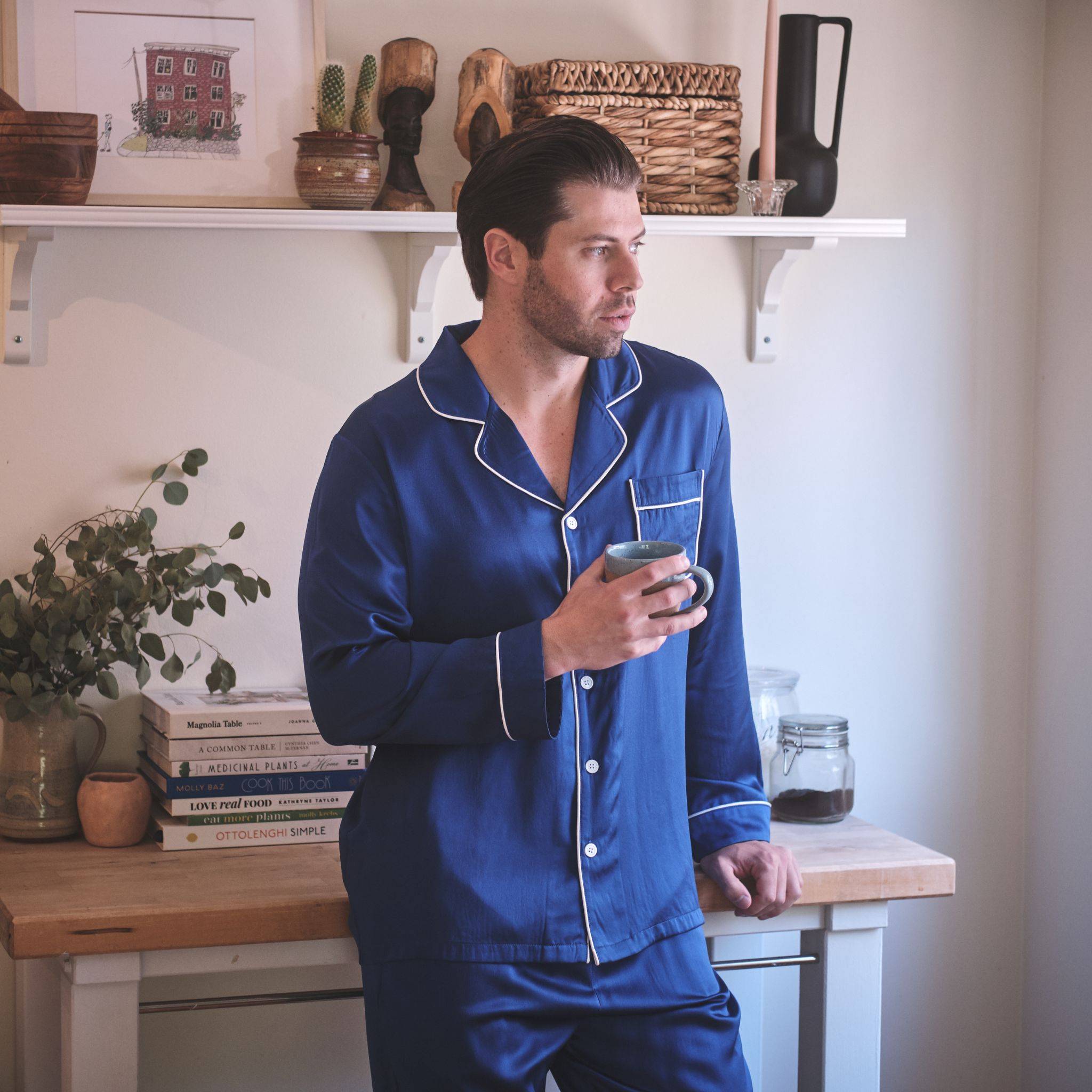 man drinking a cup of coffee in the kitchen while wearing a royal blue silk pajama set
