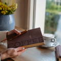 A person is holding Artebene stationery, an orange pencil case and mustard yellow book.