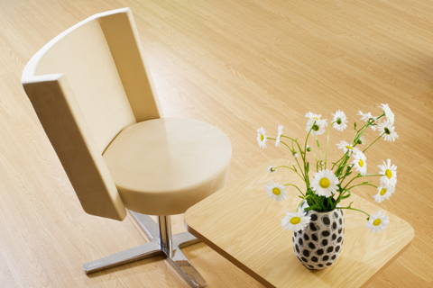 A contemporary chair and side table, sitting on a Teknoflor flooring. There is a vase with flowers on top of the side table.