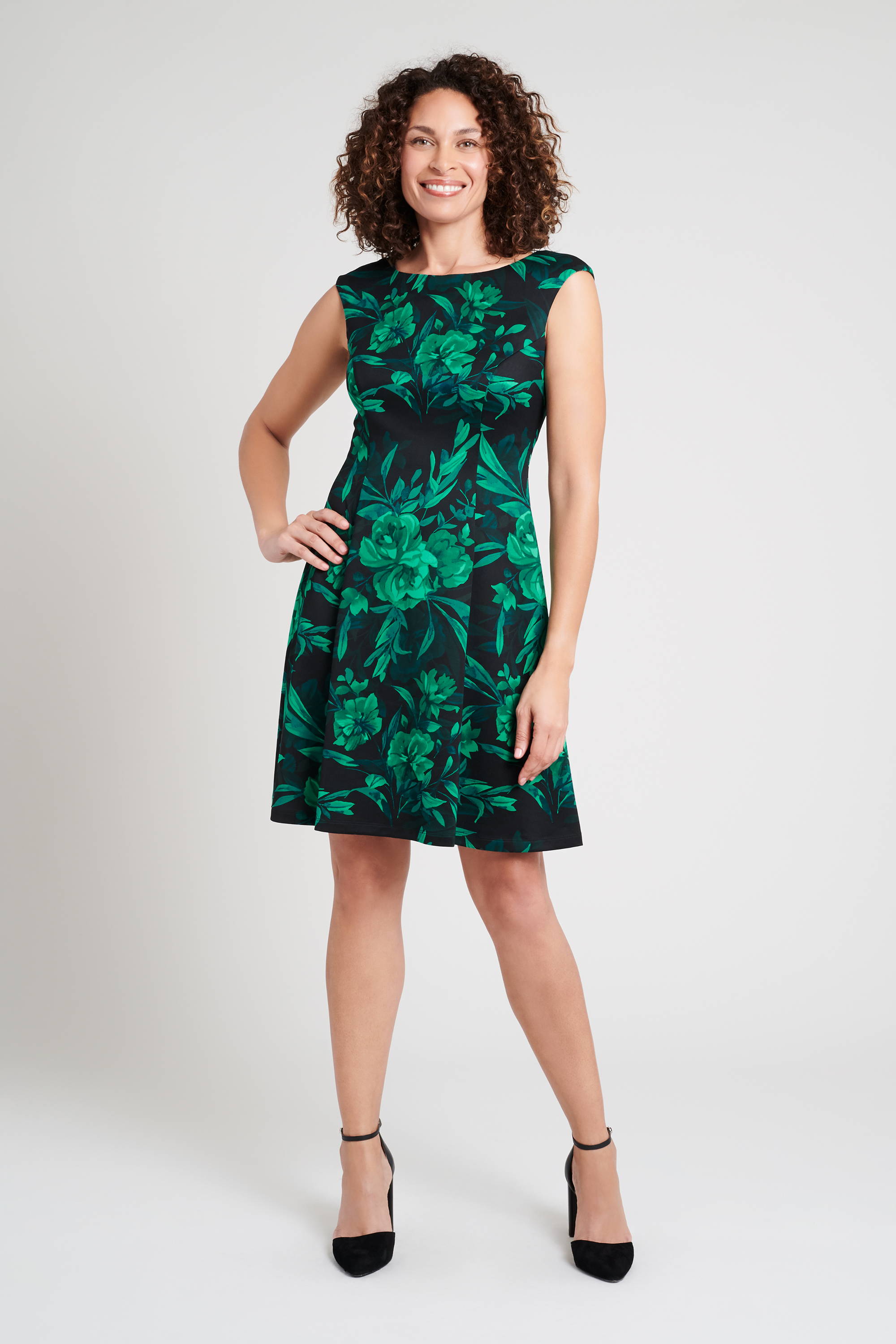 woman posing in green and black floral print sleeveless above-the-knee connected apparel dress