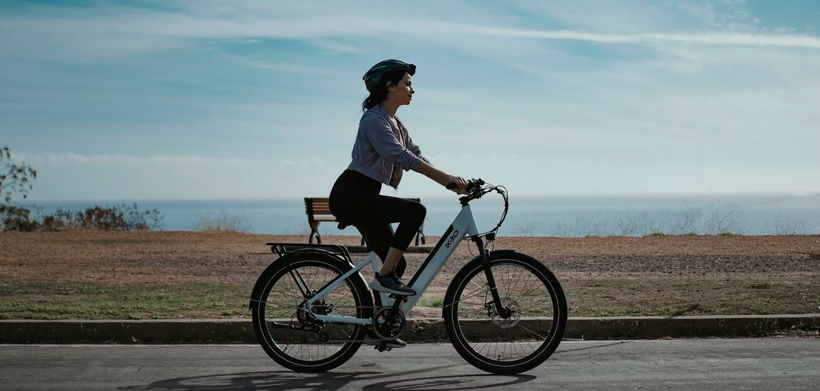 Imagen de recurso de una persona rodando encima de una bicicleta eléctrica y, al fondo, el mar.