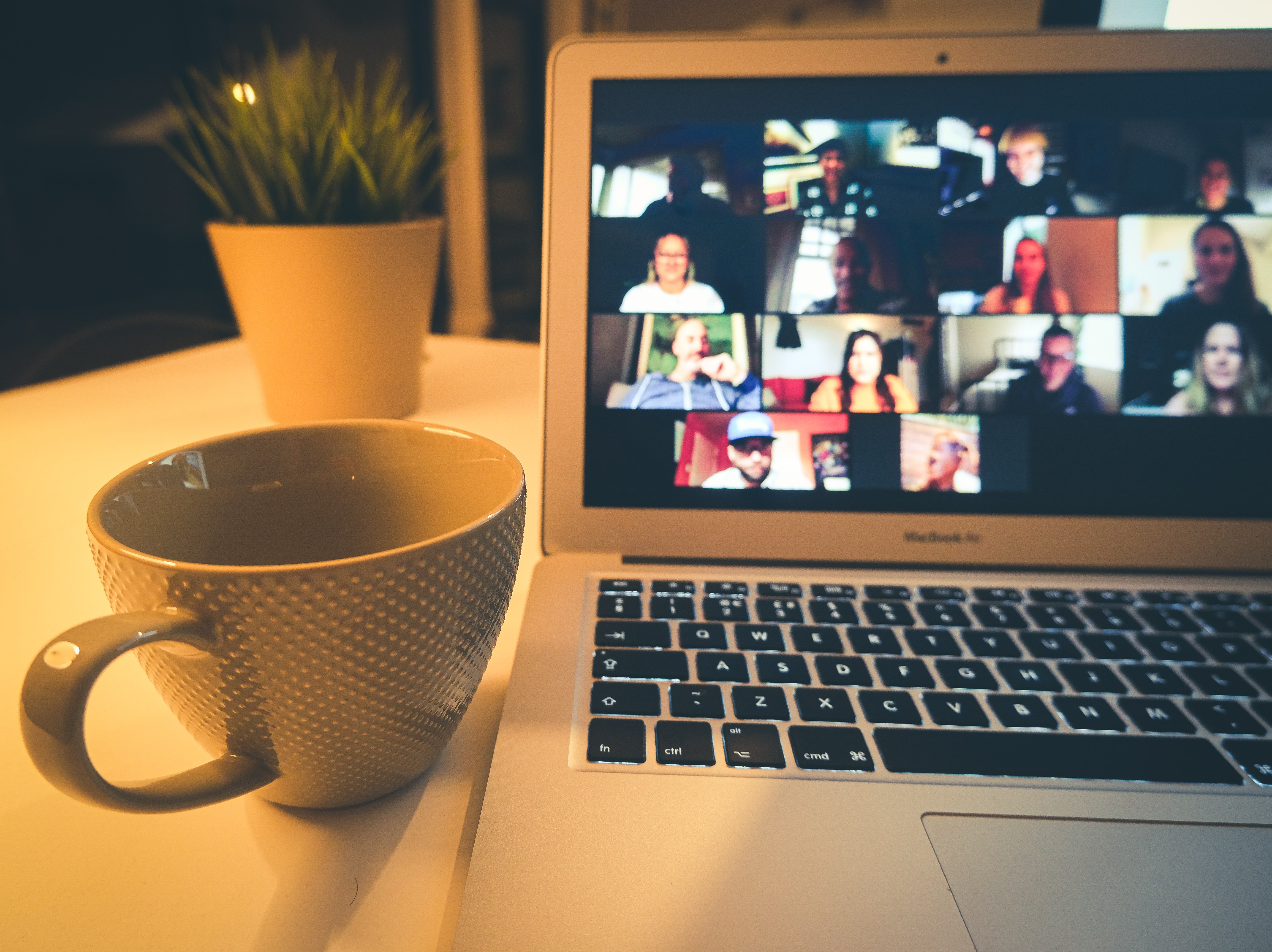 A calming scene of a laptop with several people on video chat and a coffee mug nearby.