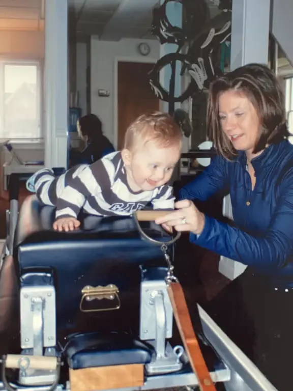 Photo of baby laying on the reformer with his mother on the side supporting. 