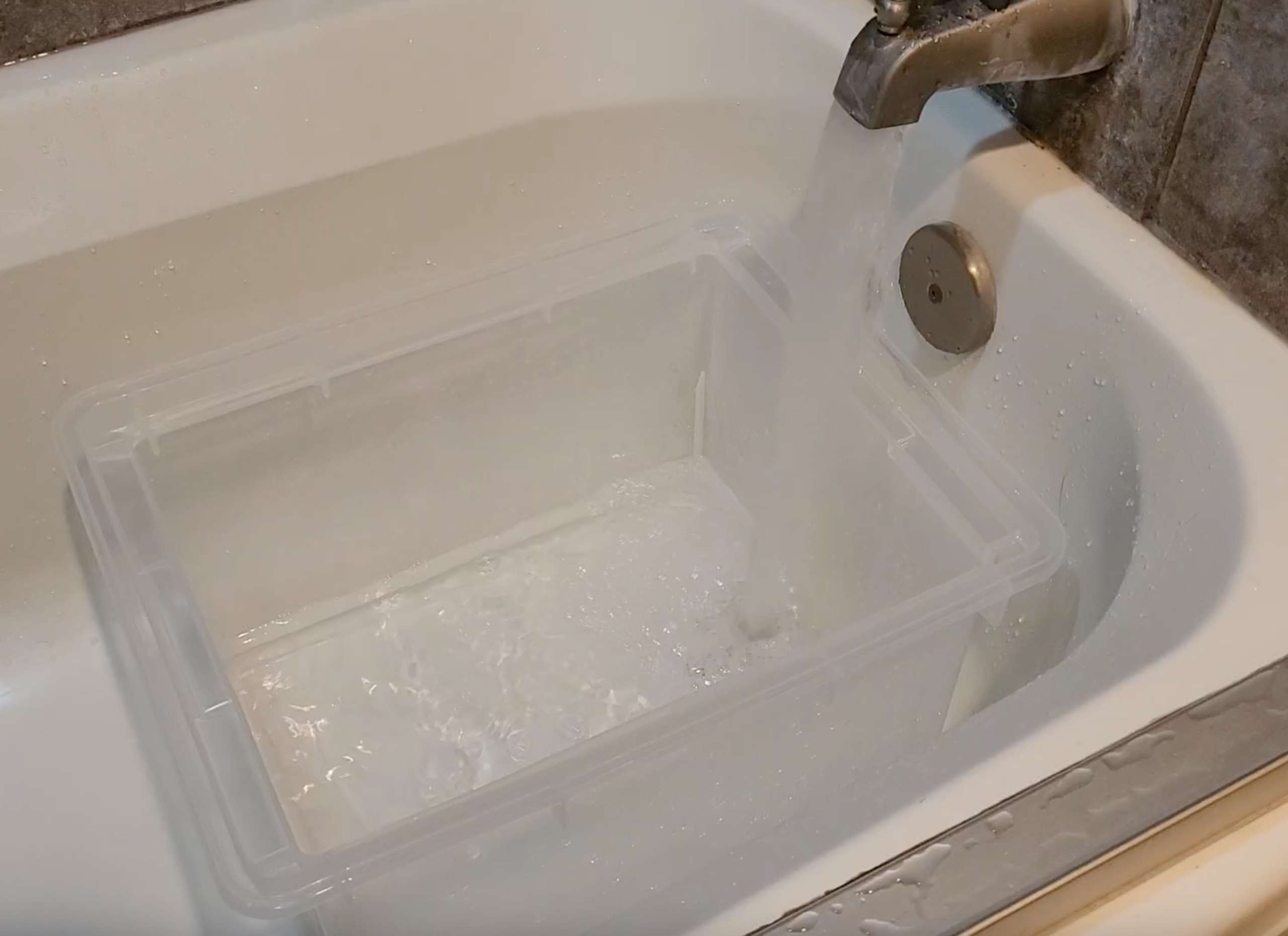 a water basin sitting in a bathtub being filled with lukewarm water from the tap