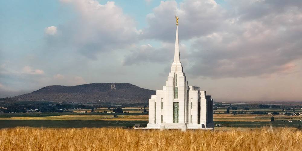 Photo of the Rexburg Temple behind an autumn field with the Rexburg hills in the background.