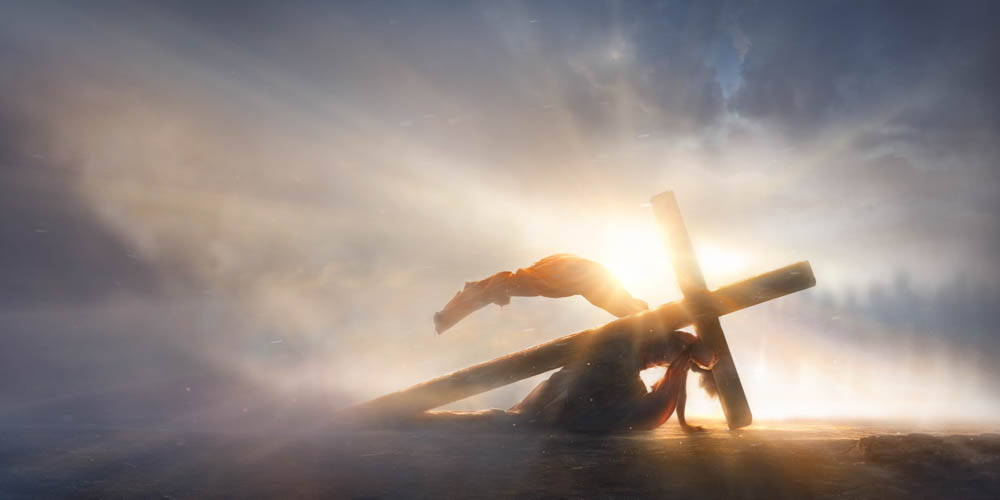Picture of Jesus crumpled beneath the weight of His cross. The sun rays shine dramatically across the surfaces of His robe and the cross.