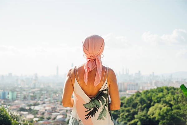 Woman with a pink head wrap looking out into a scenic view.