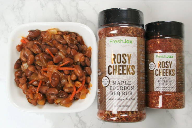 A bowl of BBQ baked beans next to a large and small bottle of FreshJax Organic Rosy Cheeks Spice Rub.
