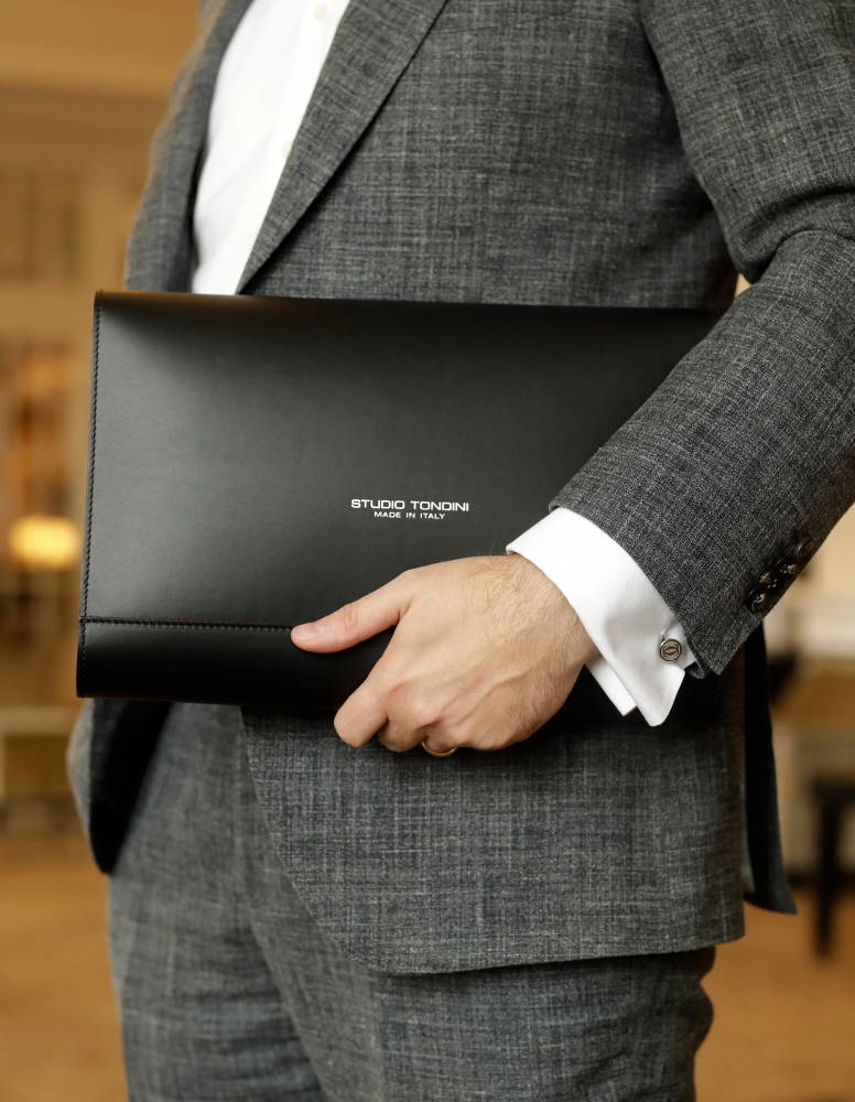 A model dressed in a suit, carrying the Studio Tondini Document Holder by hand and arm in a luxury hotel – blending sophistication and practicality in an elevated setting.