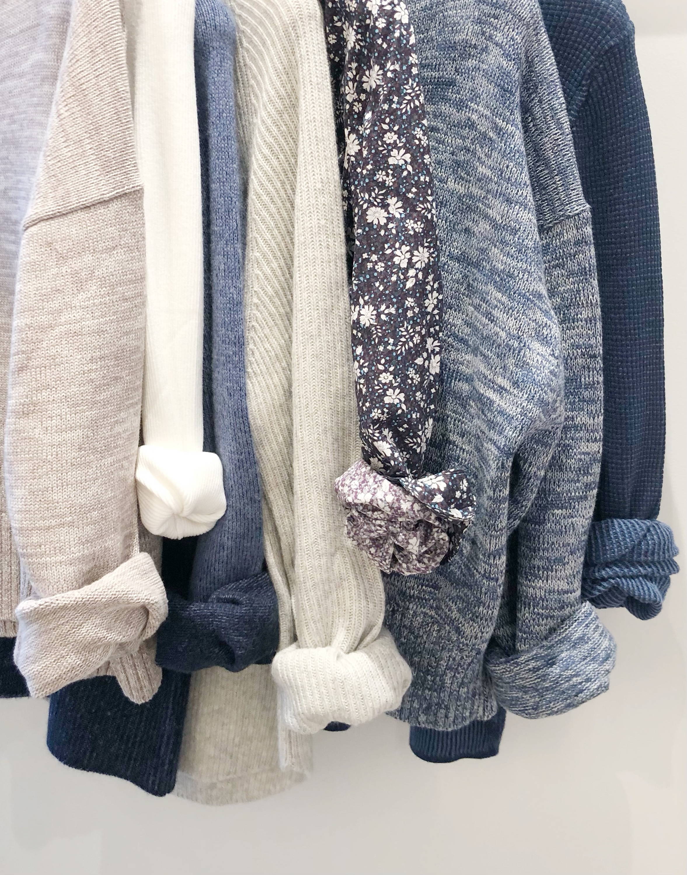 A rack of blue and grey sweaters and tops.
