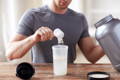 man in gray shirt adding a scoop of collagen protein to his morning shake