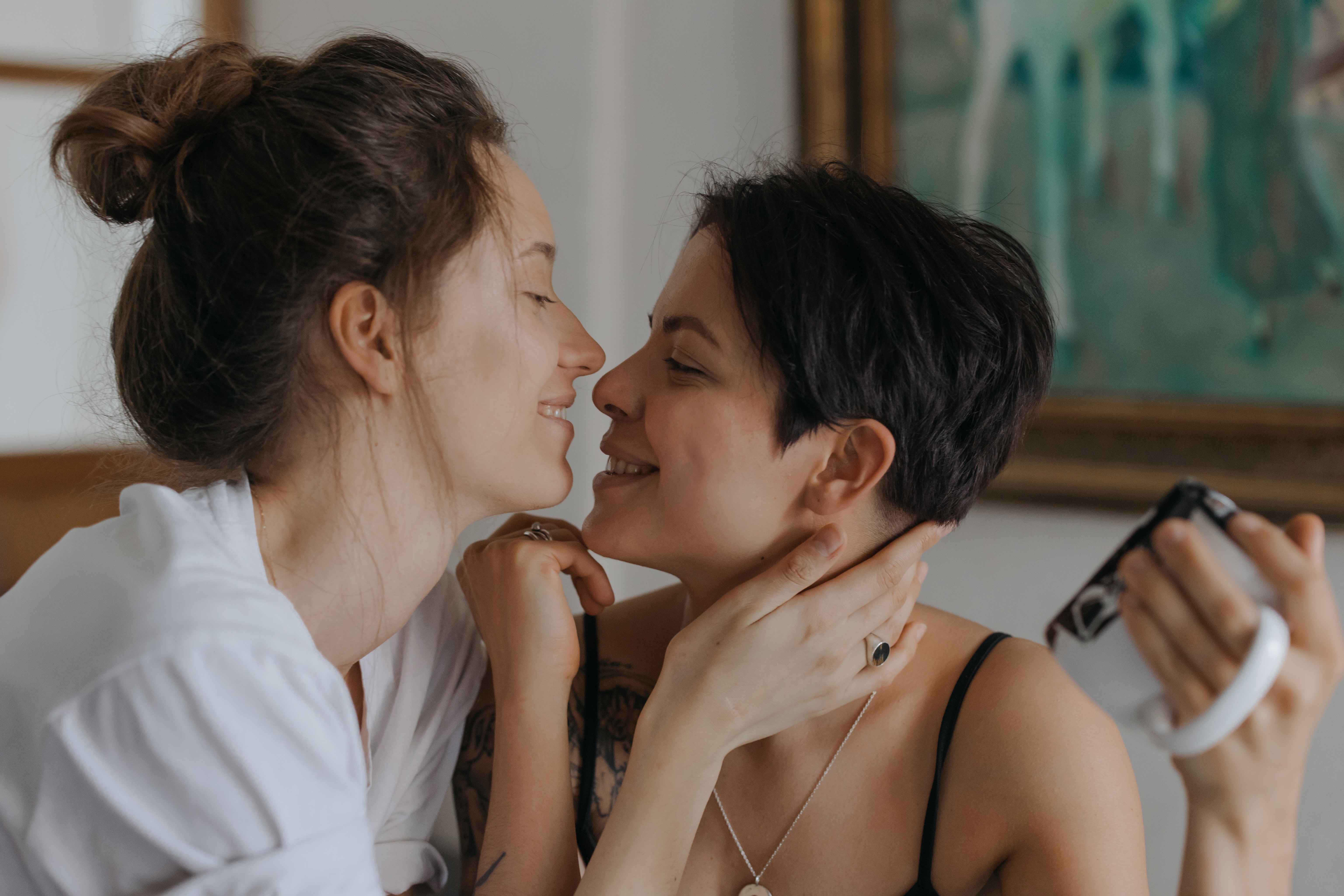 Two women, one with long the other with short hair, have their morning coffee and go in for a kiss.