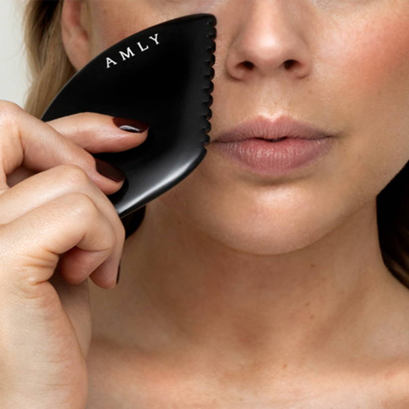 woman holds the AMLY gua sha up to her face