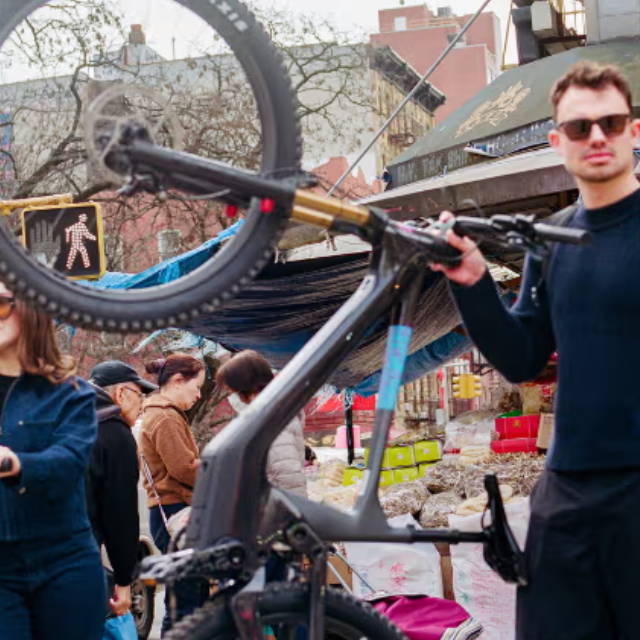a man holding a mountain bike up vertically in a crowded street
