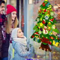 Mother, father, and daughter smiling and looking at the Montessori Christmas Tree with lights, attached to a shop window. 