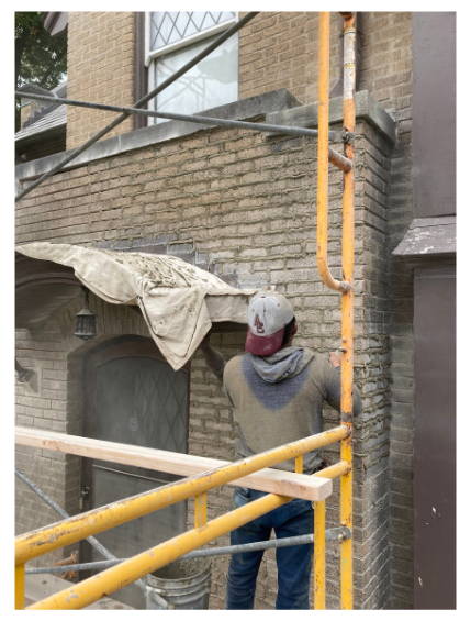 Worker performing tuckpointing on an aging brick facade of a historic building using traditional masonry tools.