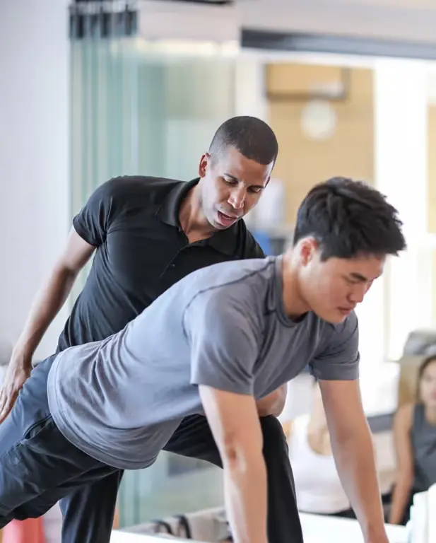 Photo of Brett helping a male student on reformer