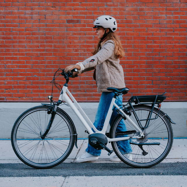 woman walking next to a Gazelle Medeo electric city bike in front of a red brick wall