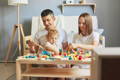 Mother, father, and their baby boy sitting next to a table full of Montessori toys and holding wooden pieces. 