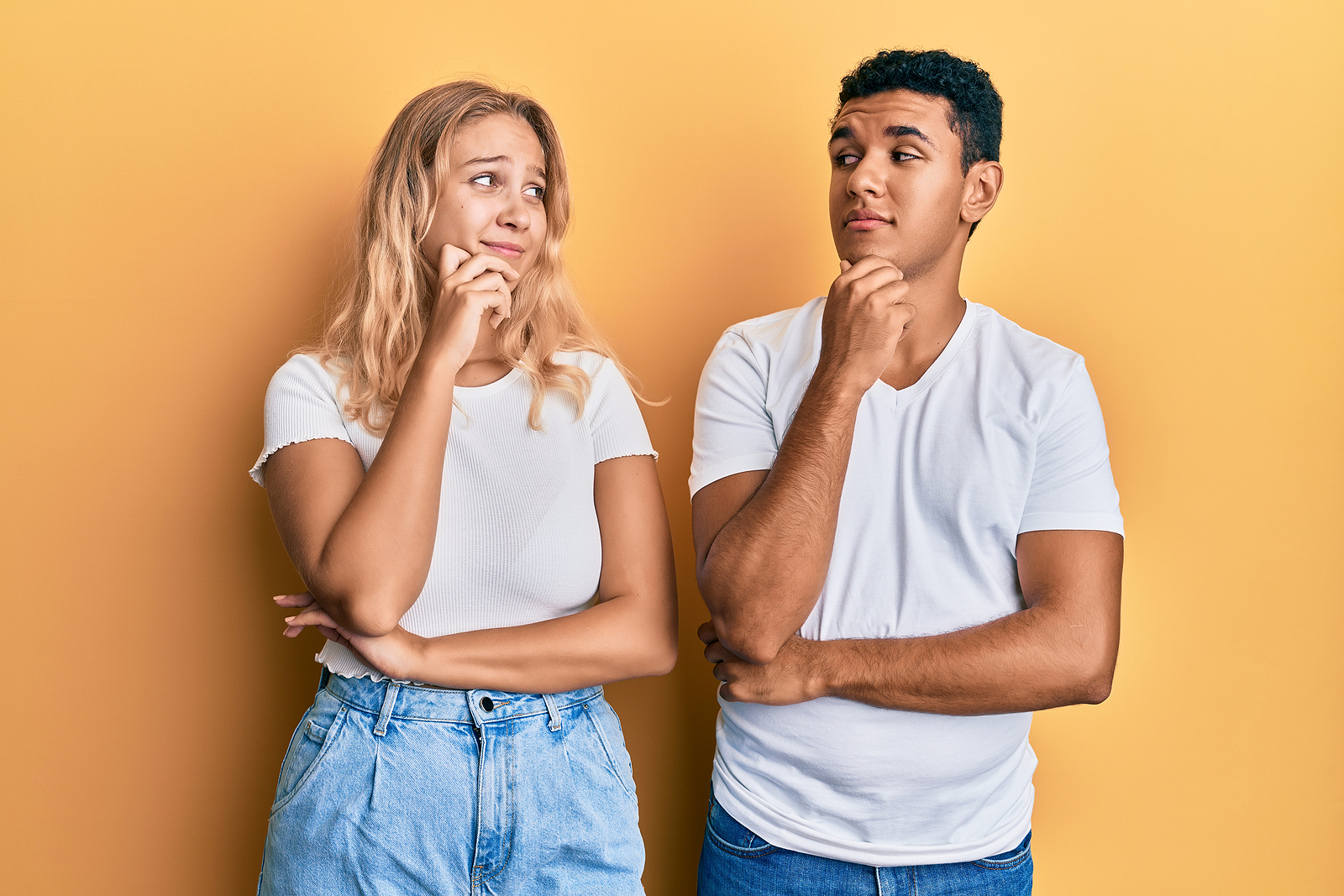 A young interracial couple wearing casual white tshirt with hand on chin thinking about question, pensive expression. smiling with thoughtful face.