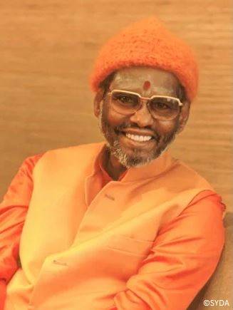 Swami Muktananada / Baba sitting and smiling wearing orange hat