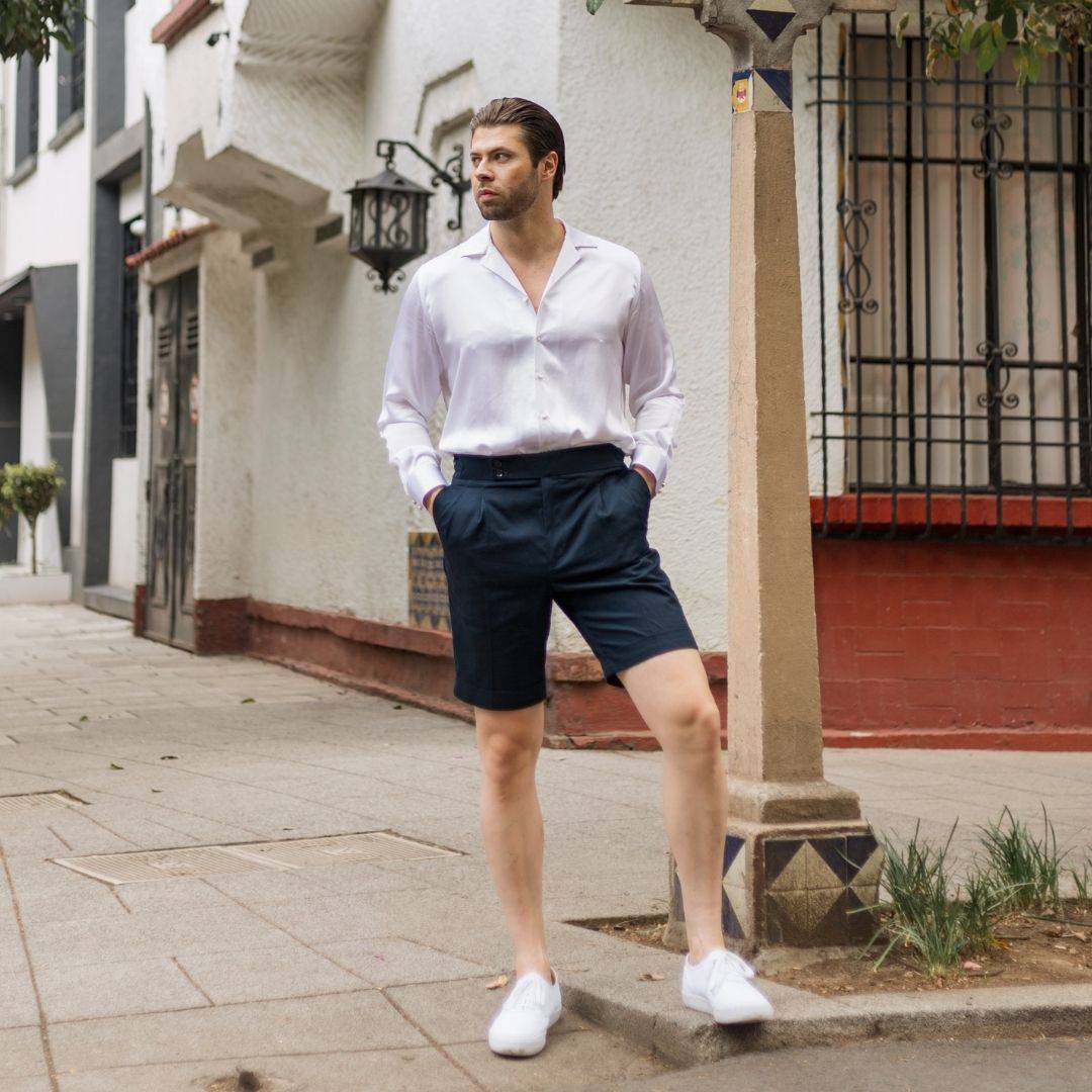 model standing on a street corner wearing white shoes blue shorts and a mens long sleeve white silk shirt from 1000 kingdoms