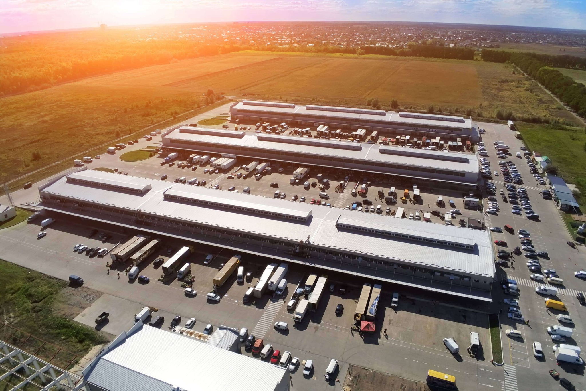 Aerial view of an industrial warehouse, integral to distribution and logistics, featuring several trucks parked in the adjacent parking lot.