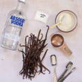 A group of items containing: a vodka bottle, vanilla beans, tablespoons, sugar and xanthan gum