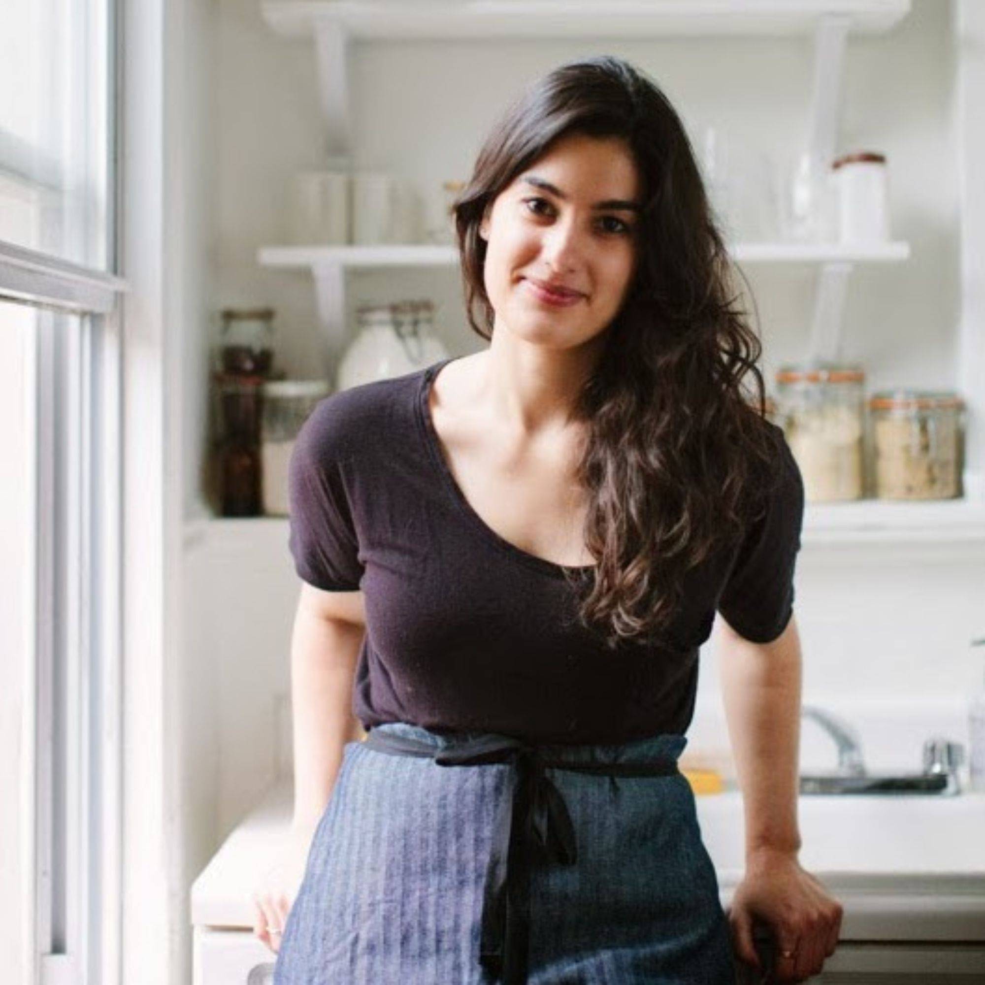 A person wearing a blue apron stands in a brightly light white kitchen