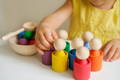 Close up of a little girl in yellow dress playing with colorful Montessori wooden pegs. 