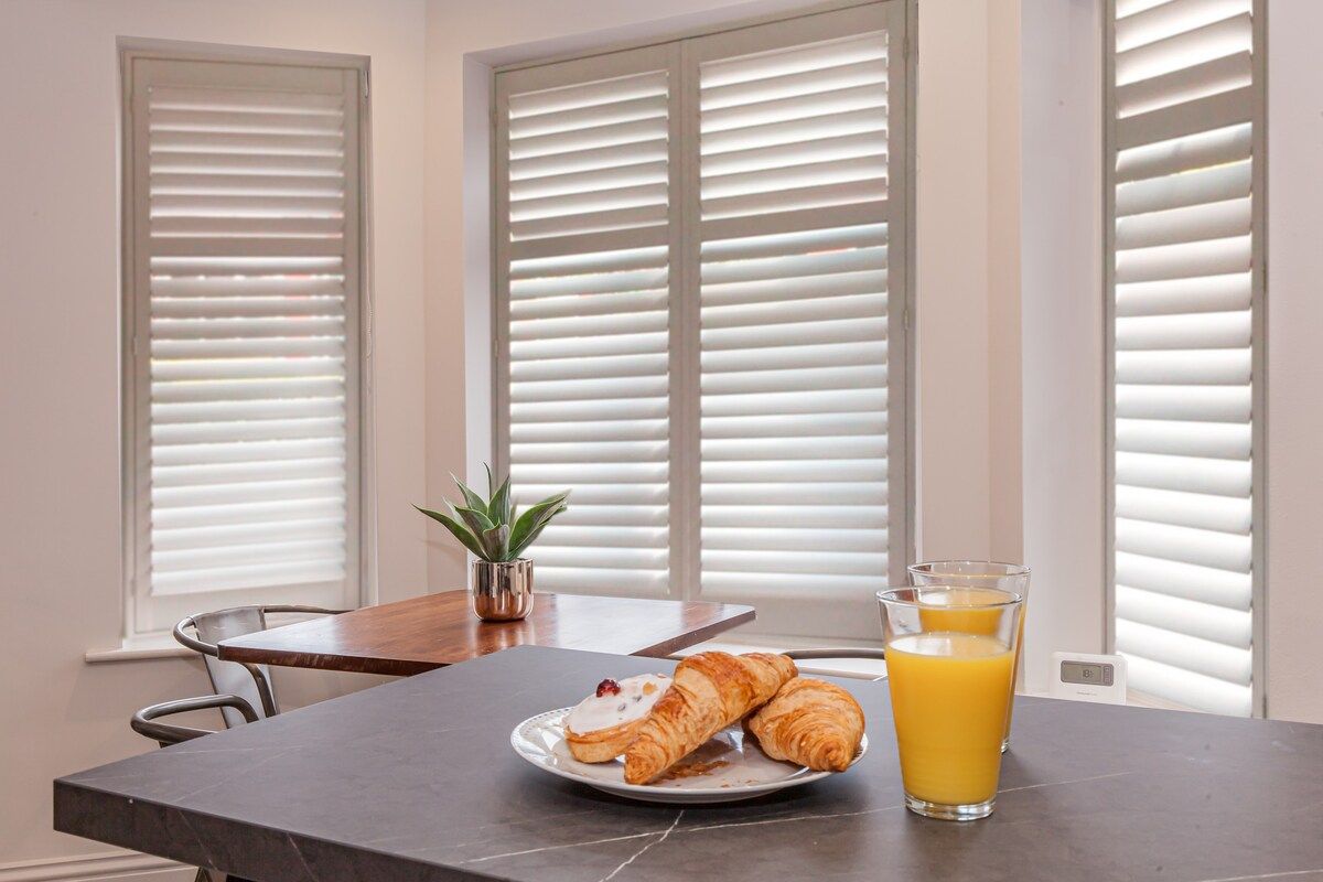 Dining table near 4 large windows with pastries and orange juice on the table