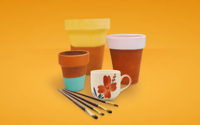 Terracotta pots painted in colorful stripes and a white mug with flowers next to some paint brushes for Confetti's Virtual Ceramic Painting