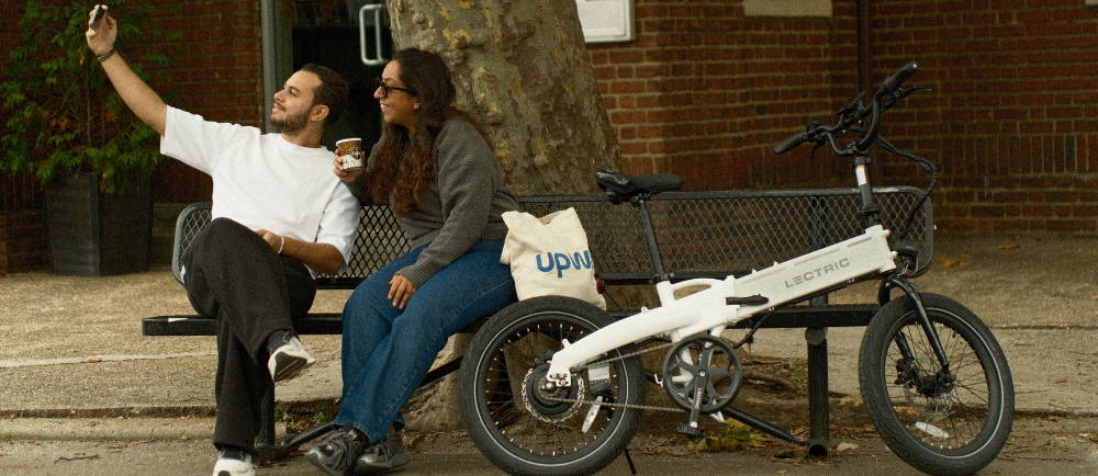 Two people on bench sitting next to Lectric electric folding bike