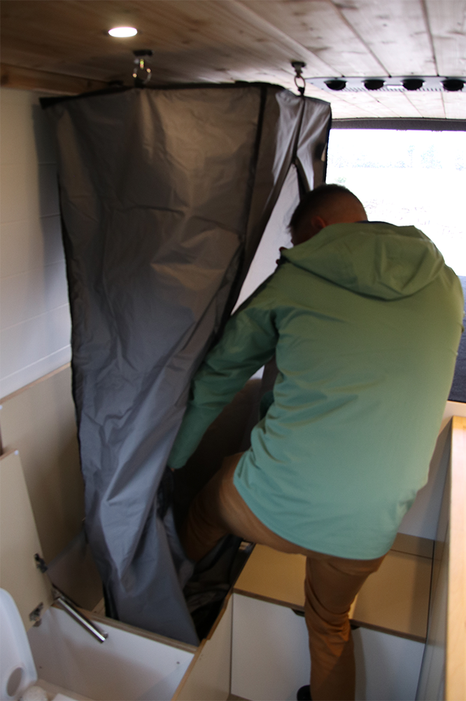 Man Stepping into Pop-Up Bench Shower in Camper Van Conversion by The Vansmith