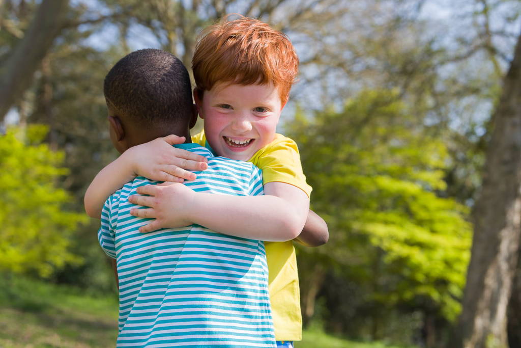 Image of two boys hugging. One with his back to us and the other smiling at the camera. They're both wearing Ducky Zebra clothes.