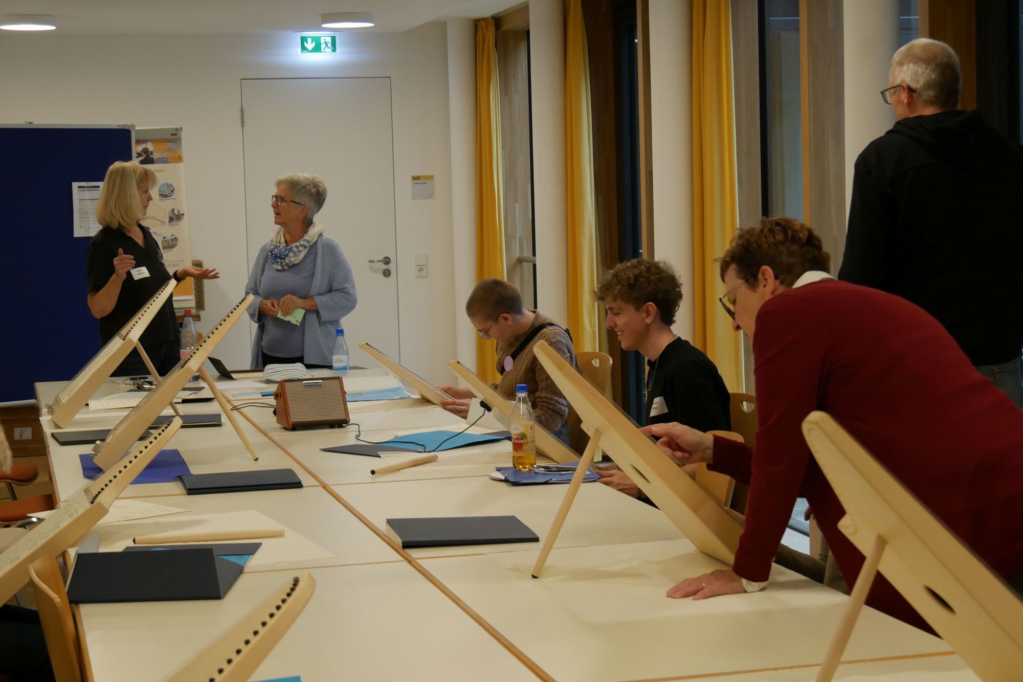 An einem Tisch sitzen einige Menschen und spielen gemeinsam auf Veeh-Harfen. 