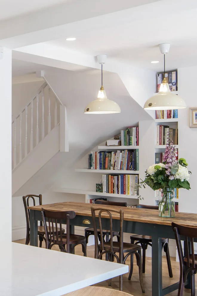 Three large Classic Cream lamps hang over a long dining table in a open kitchen plan