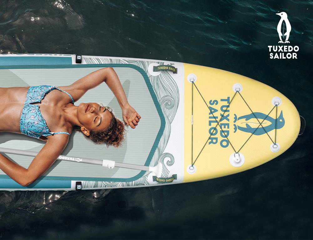 The woman is lying on the Tuxedo Sailor inflatable paddle board to enjoy the holiday time
