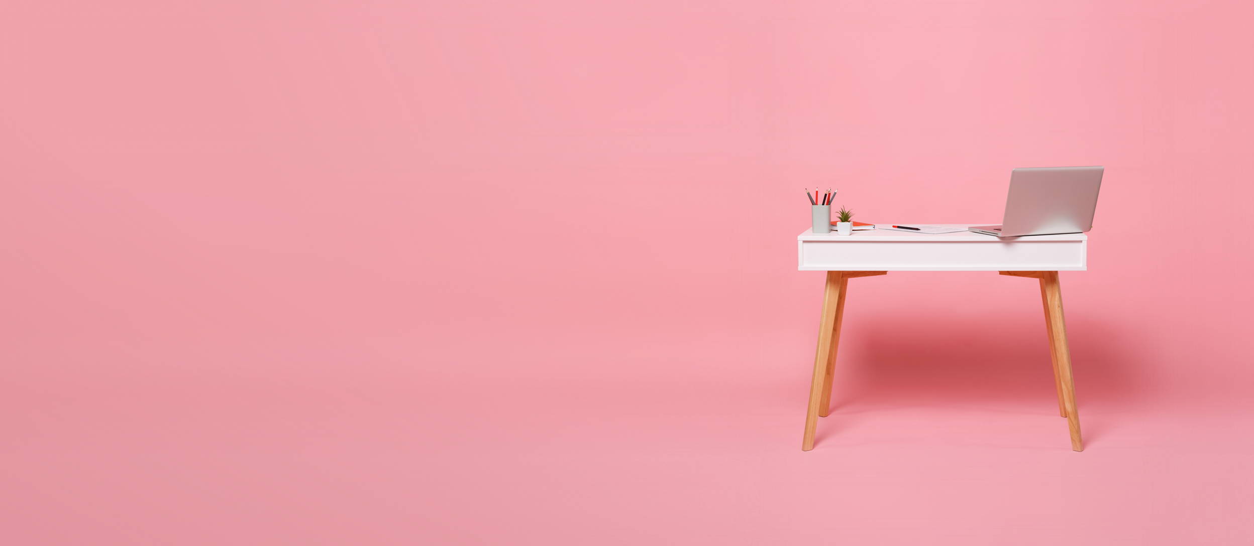 Desk with a laptop and office supplies against a pink background (large)
