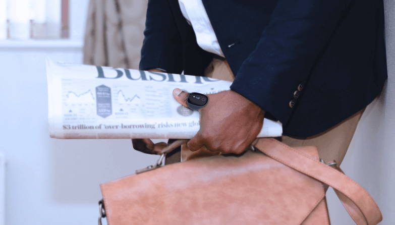 A man dresses in suit is wearing the O2 Ring and holding a newspaper on the same hand.