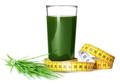 a glass of wheat grass juice next to a bundle of wheat grass clippings; a yellow measuring tape wrapped around the bottom of the glass