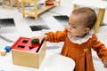 Baby girl putting wooden shapes into the object sorting box. 