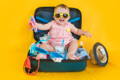 Cute baby sitting in the travel suitcase and wearing yellow sunglasses.