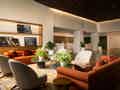 Moderne Hotellobby mit orangefarbenen Sofas, grauen Sesseln, Marmortischen und kunstvollen Dekorationen unter einer Holzdecke.