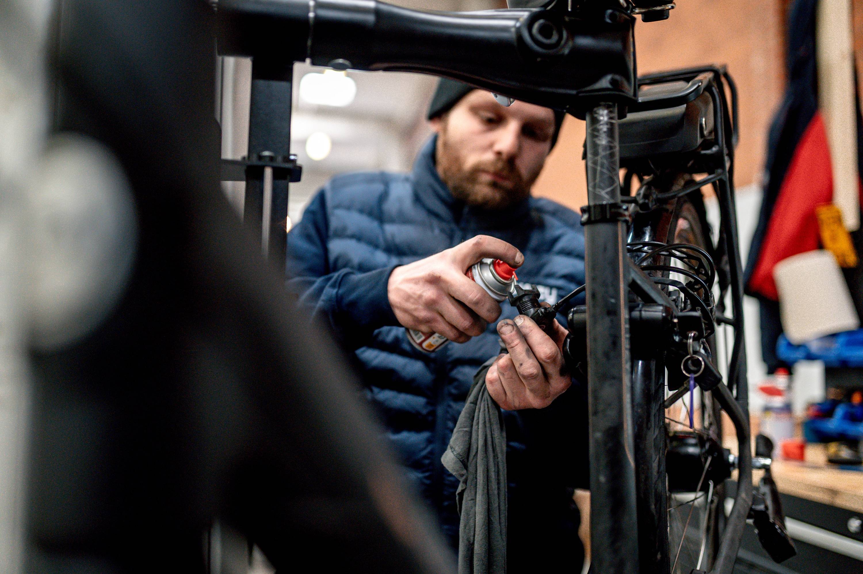 Monteur voert onderhoud uit aan elektrische fiets in werkplaats, waarbij aandrijving en kabels worden gesmeerd en gecontroleerd om slijtage te verminderen en betrouwbaarheid te vergroten.