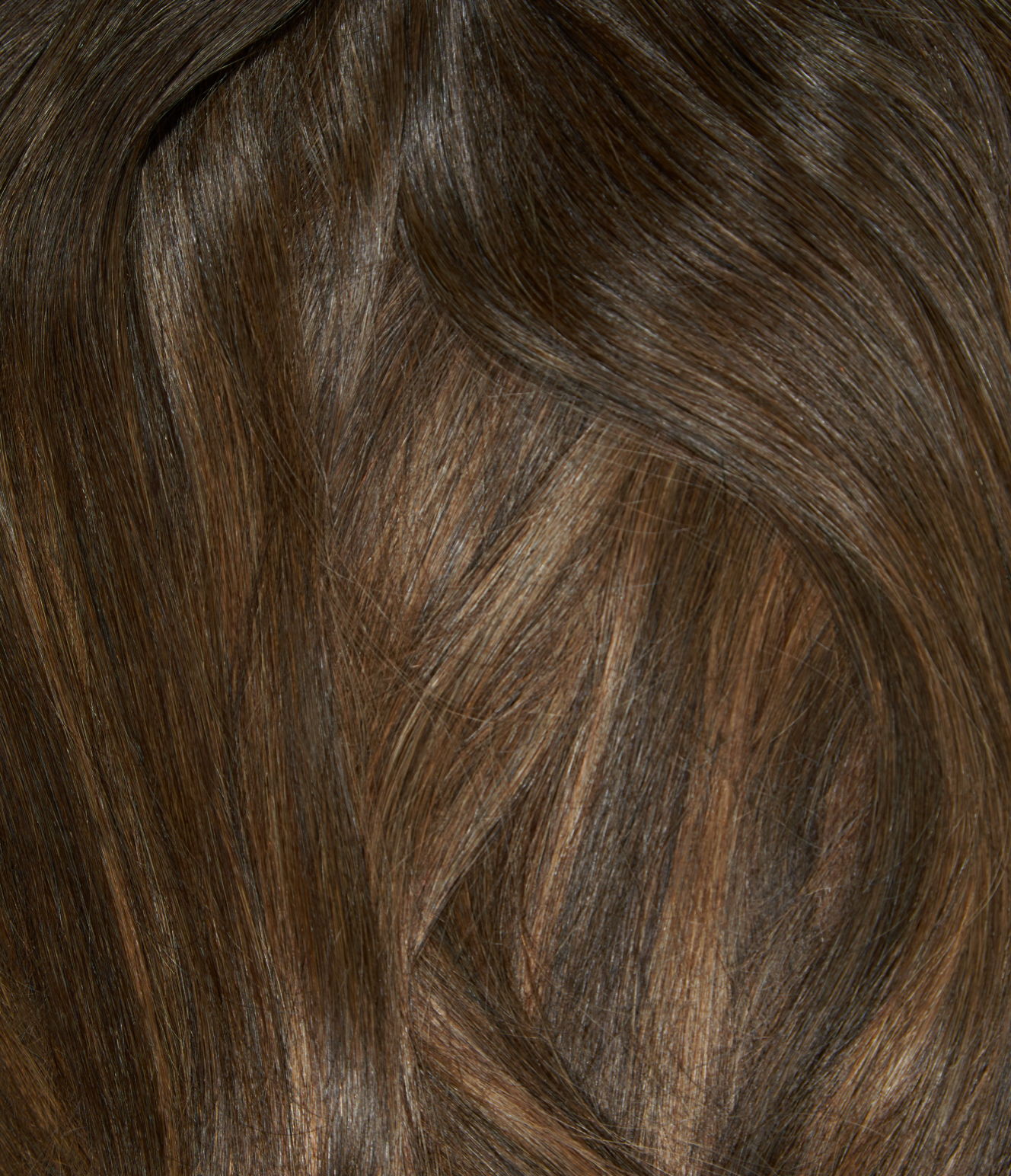 A close-up of brown hair with balayage. The hair has a subtle, graduated color that is a medium brown at the roots and is a lighter, caramel brown towards the ends.