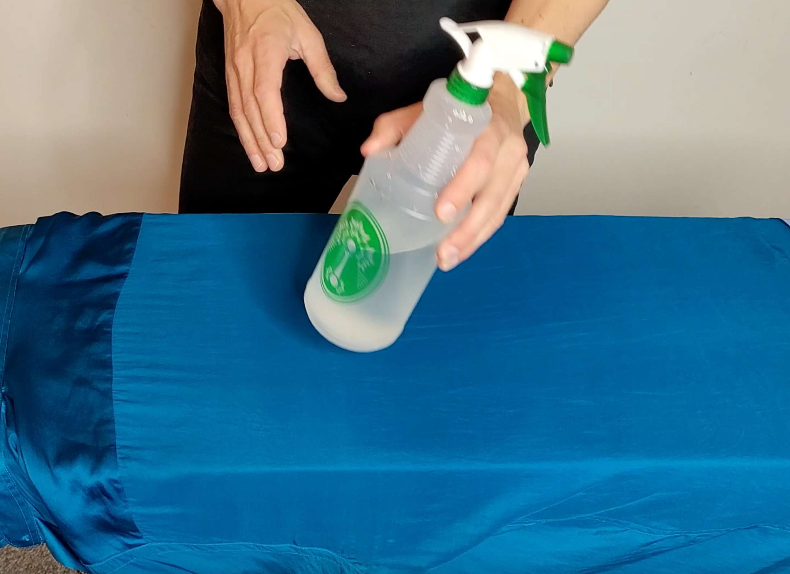 photo of a man holding a spray bottle filled with water and adding moisture to a satin shirt