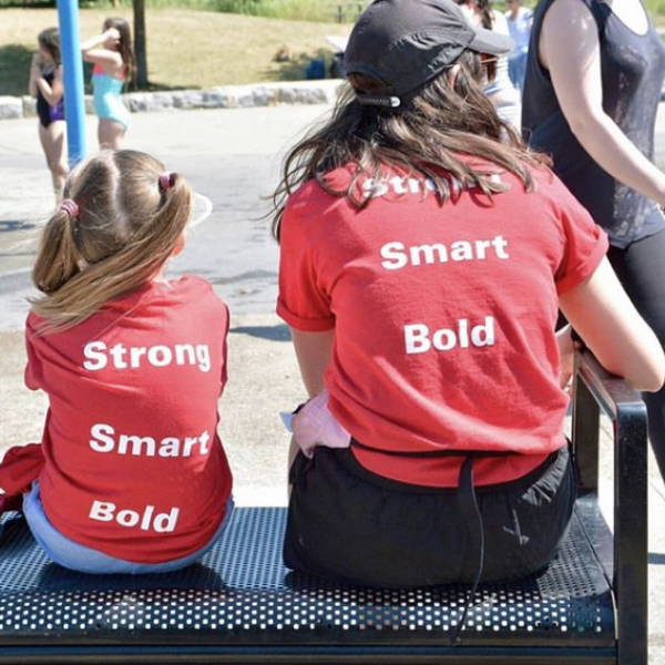 A woman and young girl sitting with shirts that say "Strong Smart Bold"